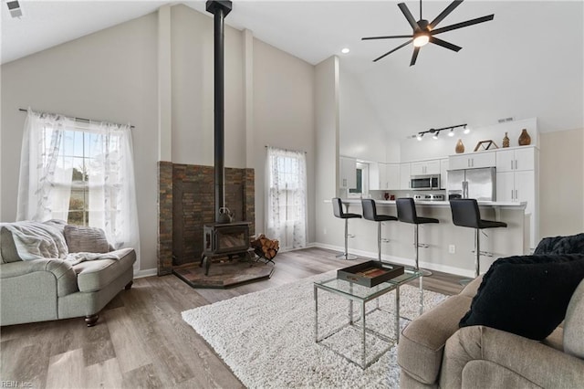 living room with baseboards, high vaulted ceiling, a wood stove, and light wood-style floors