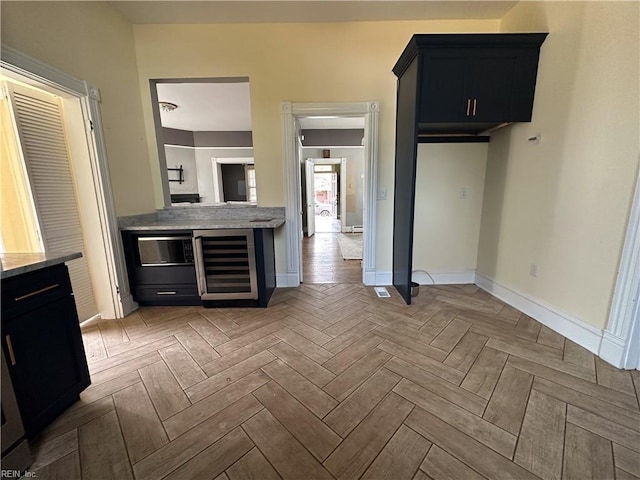 kitchen with wine cooler, baseboards, light stone counters, and dark cabinetry