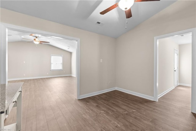 empty room with wood finished floors, visible vents, baseboards, ceiling fan, and vaulted ceiling