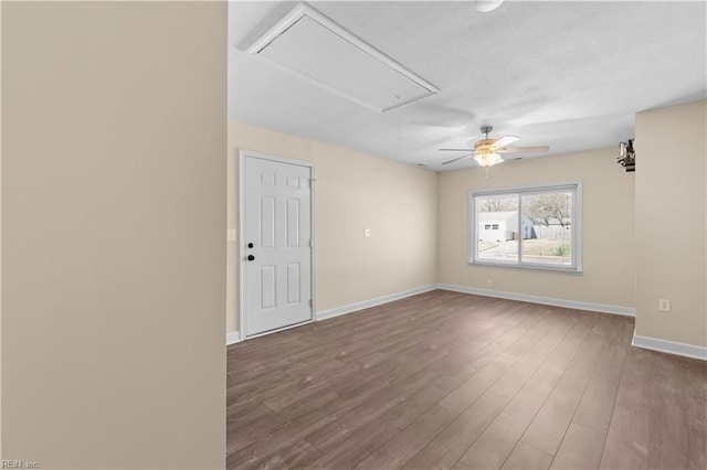 unfurnished room with a textured ceiling, attic access, baseboards, and wood finished floors