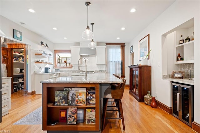 kitchen with open shelves, beverage cooler, light wood-style flooring, white cabinetry, and a sink