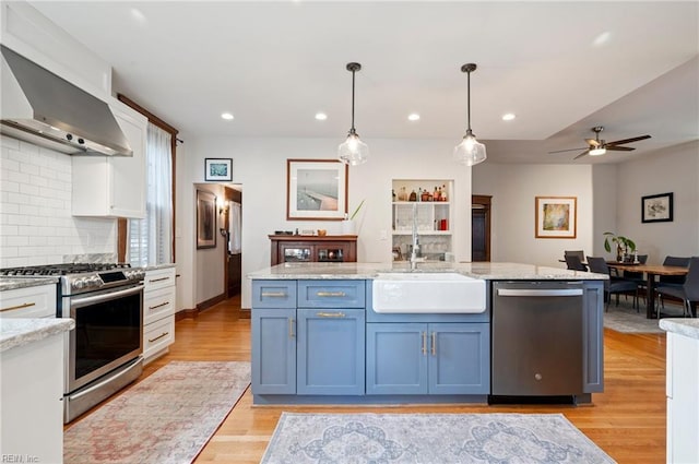 kitchen with light wood-type flooring, a sink, backsplash, stainless steel appliances, and wall chimney range hood