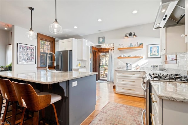 kitchen with light stone countertops, stainless steel appliances, white cabinets, light wood-style floors, and wall chimney exhaust hood