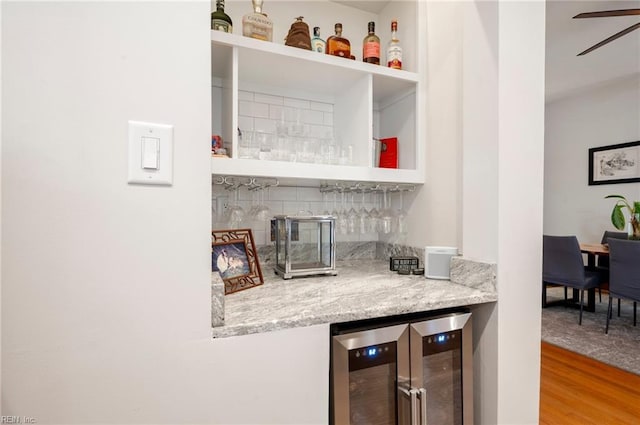 bar featuring wood finished floors, beverage cooler, ceiling fan, a bar, and backsplash