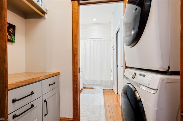 clothes washing area featuring light wood finished floors, cabinet space, and stacked washer / dryer