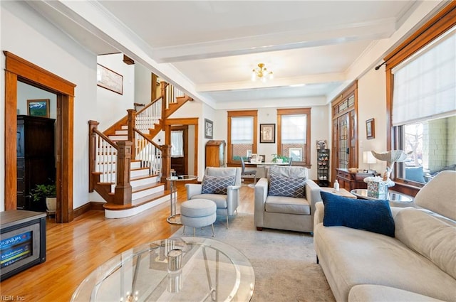 living area with beam ceiling, ornamental molding, light wood-style floors, baseboards, and stairs