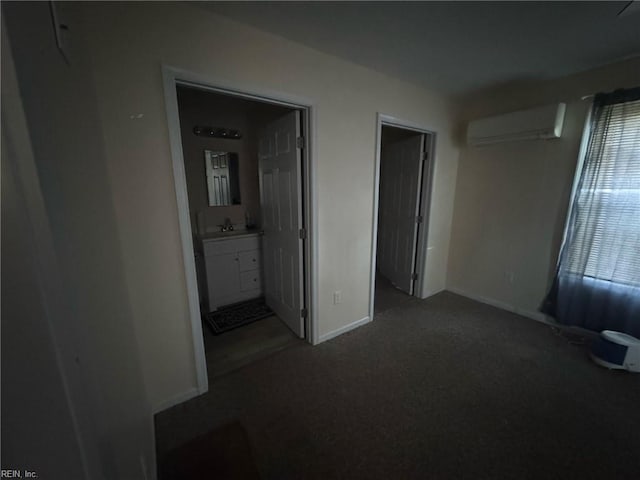 unfurnished bedroom featuring ensuite bathroom, a sink, baseboards, a wall mounted AC, and dark carpet