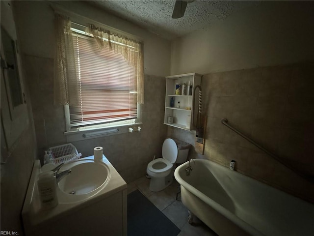 bathroom with a textured ceiling, a tub to relax in, toilet, a ceiling fan, and tile patterned floors