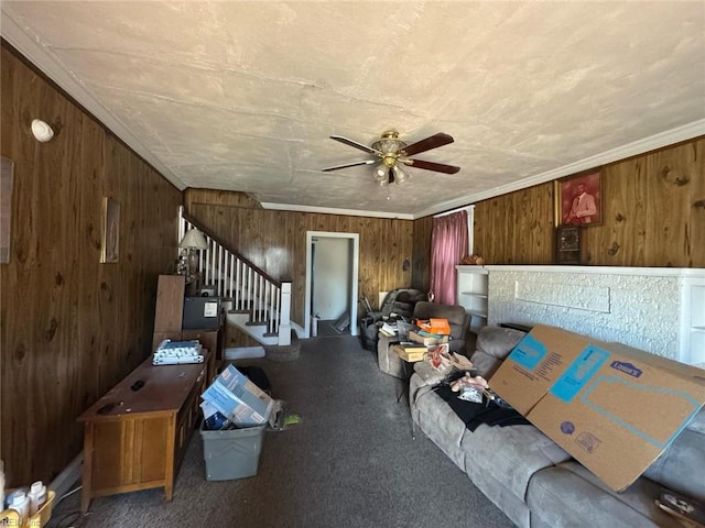 unfurnished living room featuring ceiling fan, wood walls, carpet flooring, stairs, and ornamental molding