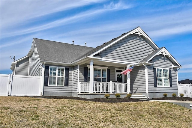 view of front facade featuring covered porch, a shingled roof, a front yard, and fence