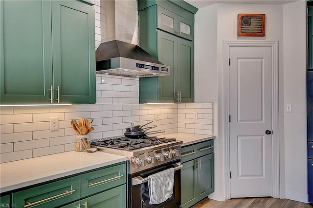 kitchen with green cabinets, stainless steel range with gas stovetop, wall chimney exhaust hood, and decorative backsplash