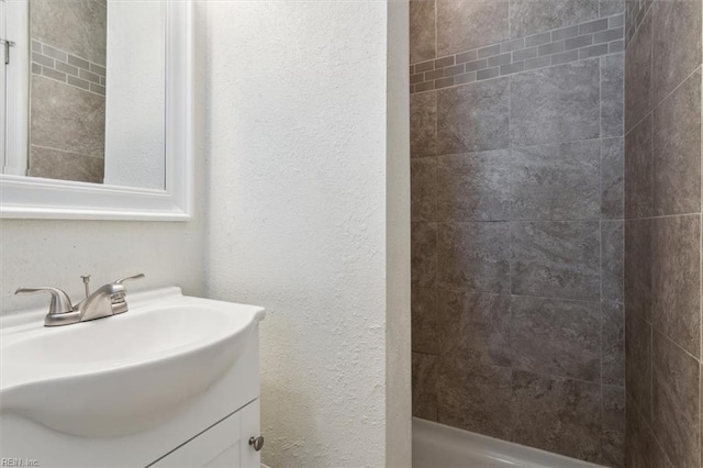 bathroom featuring vanity, walk in shower, and a textured wall