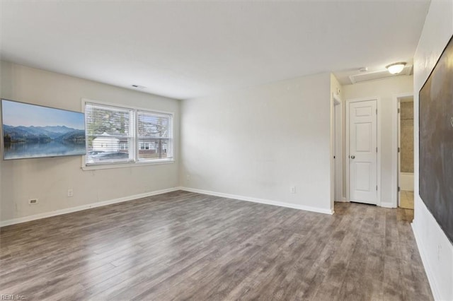 unfurnished room featuring attic access, baseboards, and wood finished floors