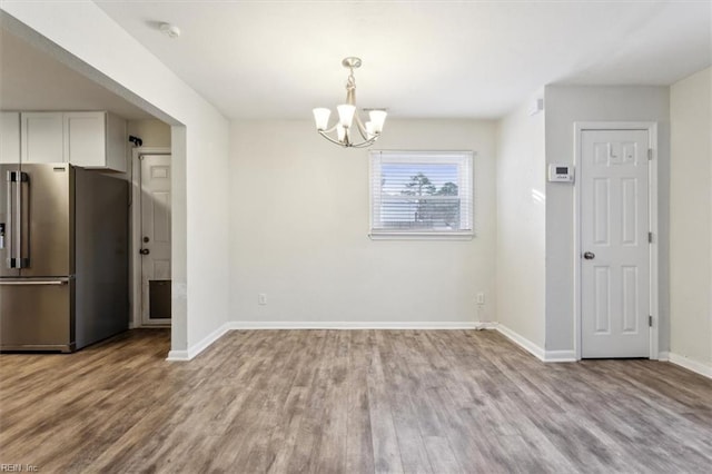 unfurnished dining area with wood finished floors, baseboards, and a chandelier