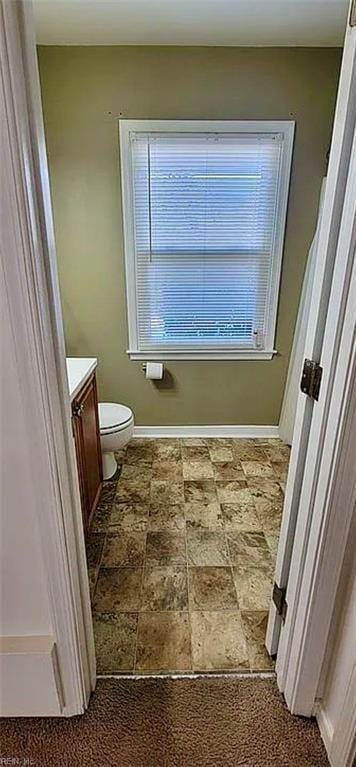 bathroom with toilet, stone finish flooring, baseboards, and vanity