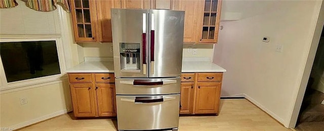 kitchen featuring brown cabinetry, glass insert cabinets, stainless steel refrigerator with ice dispenser, and light countertops