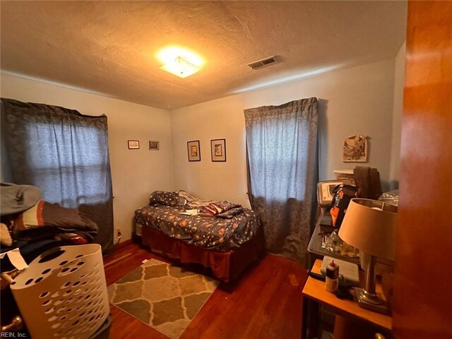bedroom with visible vents, a textured ceiling, and wood finished floors