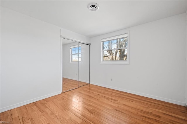 unfurnished bedroom with visible vents, a closet, light wood-style flooring, and baseboards