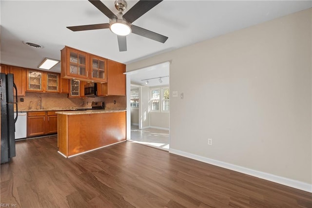 kitchen featuring decorative backsplash, dark wood-style floors, brown cabinets, stainless steel appliances, and a sink