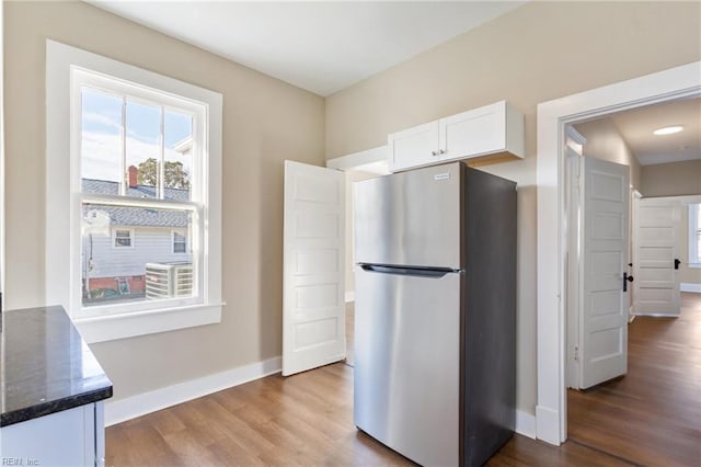 kitchen with baseboards, dark stone countertops, freestanding refrigerator, wood finished floors, and white cabinets