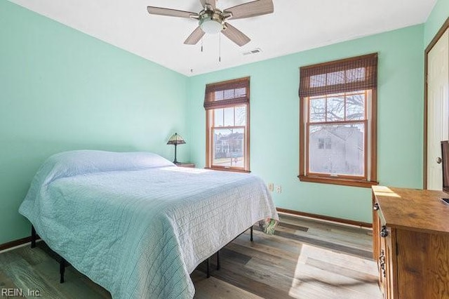 bedroom with a ceiling fan, wood finished floors, visible vents, and baseboards