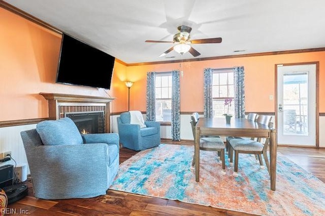 living area with a brick fireplace, wood finished floors, a ceiling fan, and ornamental molding