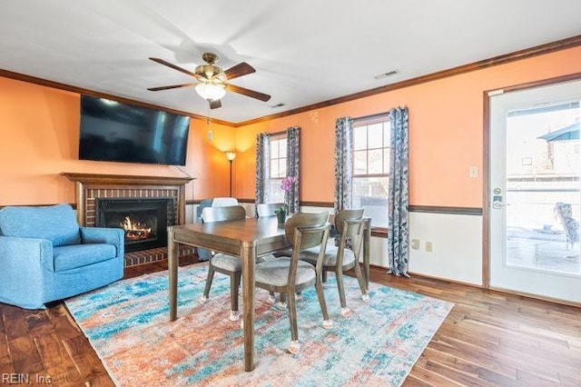 dining room with a brick fireplace, crown molding, ceiling fan, and wood finished floors