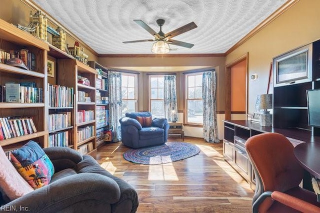 living area featuring wood finished floors, a textured ceiling, ornamental molding, and a ceiling fan