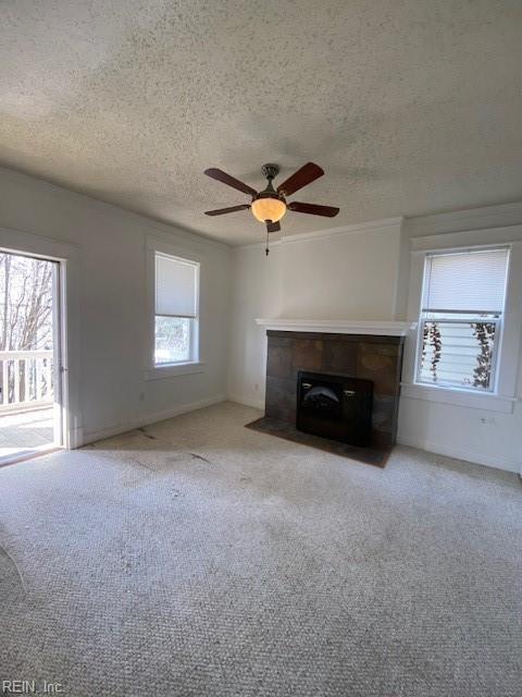 unfurnished living room with a textured ceiling, a fireplace, carpet floors, and a healthy amount of sunlight