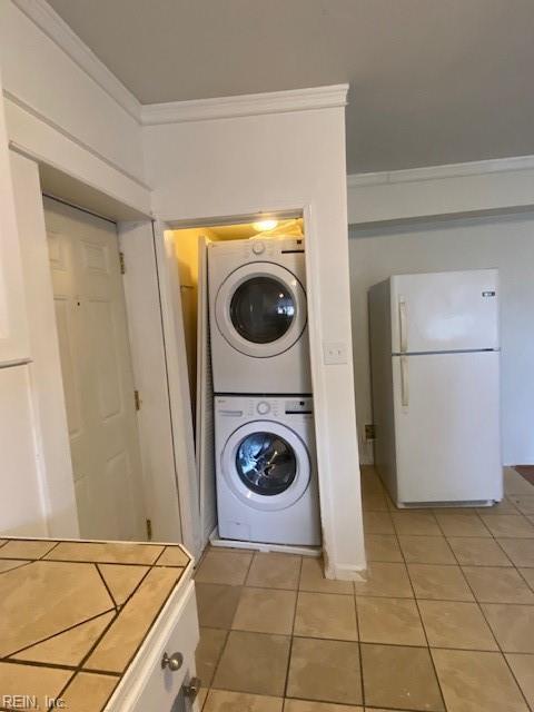 laundry area featuring laundry area, ornamental molding, light tile patterned flooring, and stacked washing maching and dryer