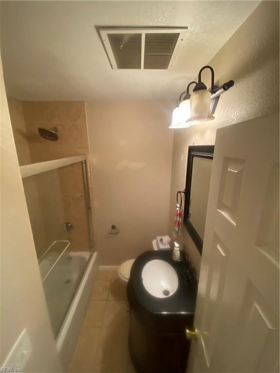 full bath featuring visible vents, bath / shower combo with glass door, a sink, tile patterned flooring, and toilet