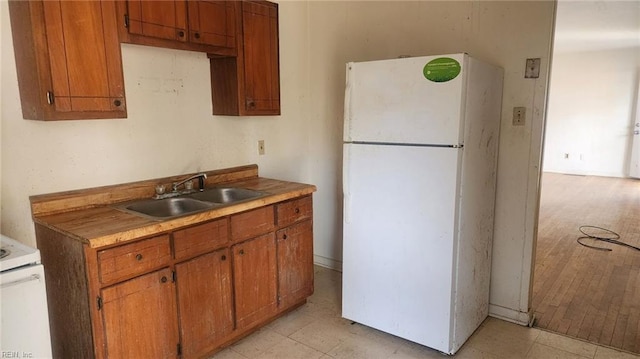 kitchen with brown cabinets, a sink, freestanding refrigerator, light countertops, and stove