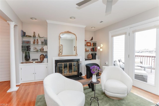 living room featuring decorative columns, light wood-style floors, and a glass covered fireplace