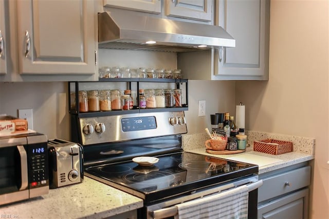 kitchen with under cabinet range hood, light stone counters, appliances with stainless steel finishes, and gray cabinetry