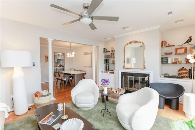 living area featuring a glass covered fireplace, crown molding, wood finished floors, and ornate columns