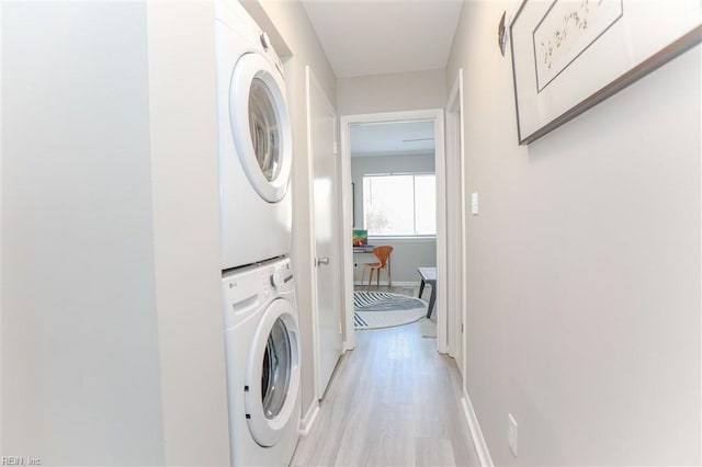 clothes washing area with laundry area, baseboards, light wood-style floors, and stacked washer and dryer