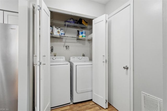 laundry room with laundry area, light wood-style flooring, washing machine and dryer, and visible vents