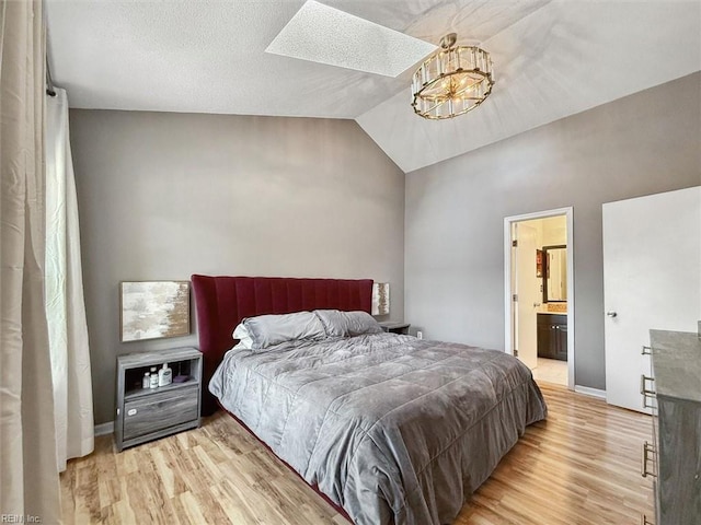 bedroom featuring baseboards, vaulted ceiling with skylight, light wood-style floors, and ensuite bathroom