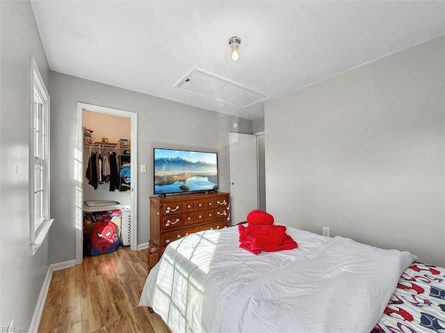 bedroom featuring attic access, wood finished floors, baseboards, and a closet