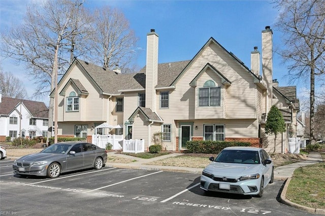 view of property with brick siding, uncovered parking, and fence