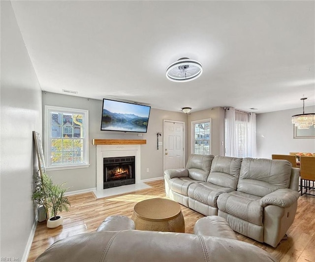 living area featuring a fireplace with flush hearth, baseboards, visible vents, and light wood finished floors