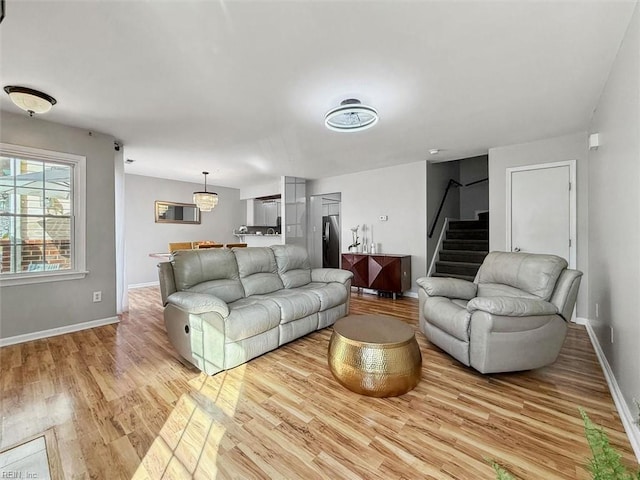 living room featuring light wood-type flooring, baseboards, and stairs