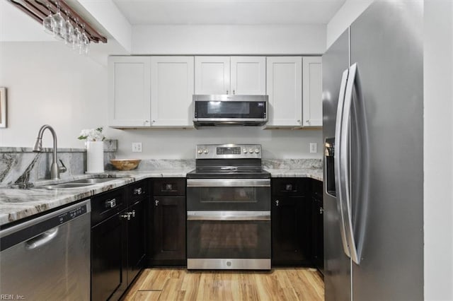 kitchen featuring a sink, appliances with stainless steel finishes, white cabinets, light wood finished floors, and light stone countertops