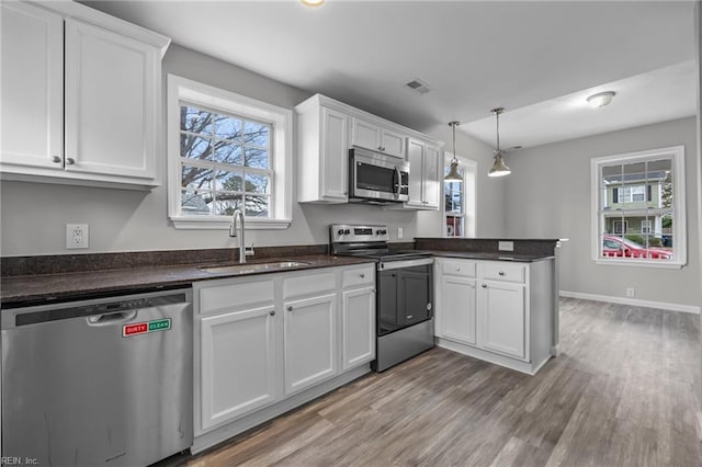 kitchen featuring wood finished floors, a peninsula, a sink, white cabinets, and appliances with stainless steel finishes