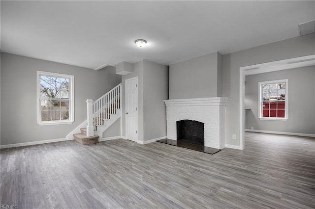 unfurnished living room with stairs, a brick fireplace, wood finished floors, and baseboards