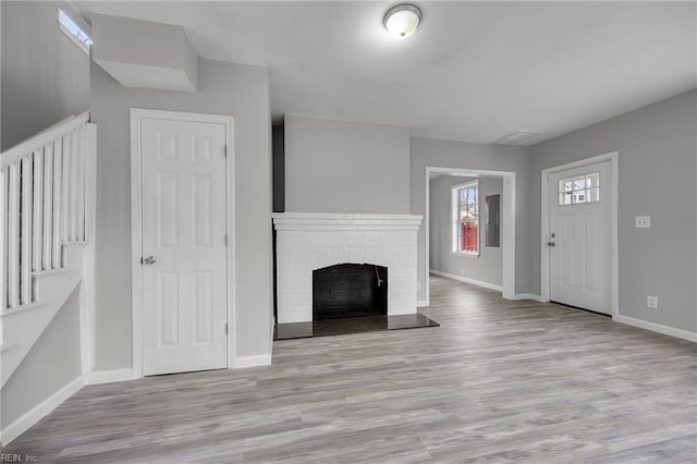 unfurnished living room with baseboards, a brick fireplace, and wood finished floors