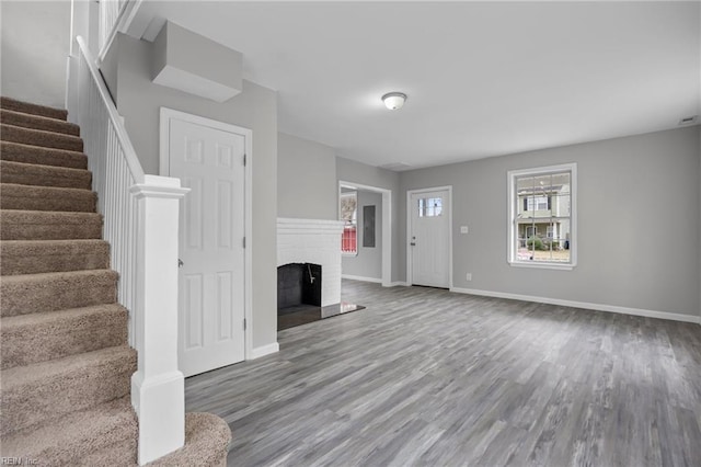 unfurnished living room featuring a brick fireplace, stairs, baseboards, and wood finished floors