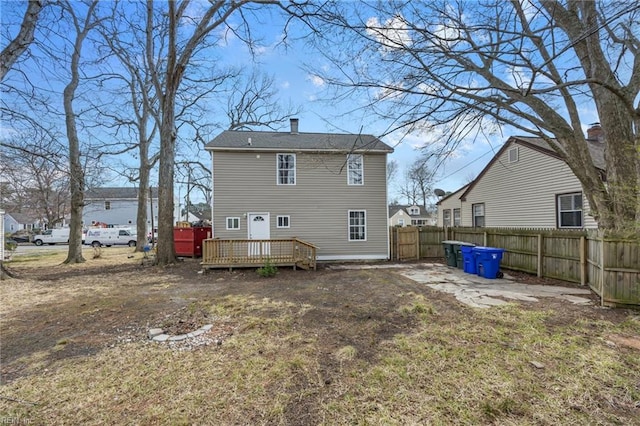 rear view of house with a wooden deck, a chimney, and fence