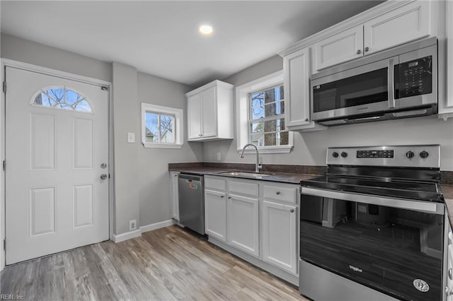 kitchen featuring dark countertops, light wood-style flooring, appliances with stainless steel finishes, white cabinets, and a sink