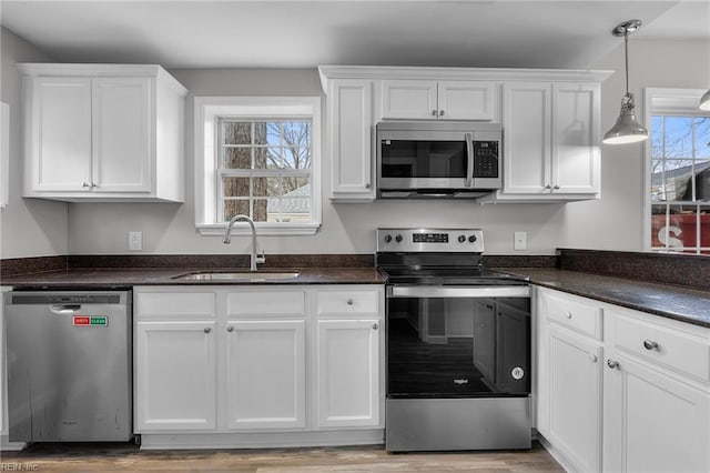 kitchen with pendant lighting, appliances with stainless steel finishes, wood finished floors, white cabinetry, and a sink